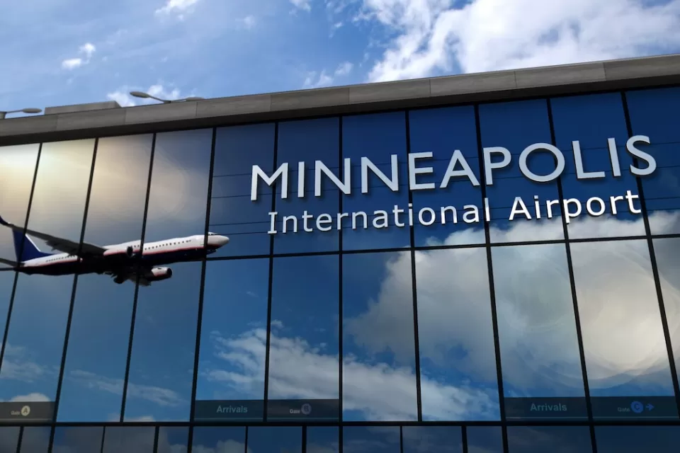 Sign on glass building for Minneapolis International Airport with airplane landing reflected in building.